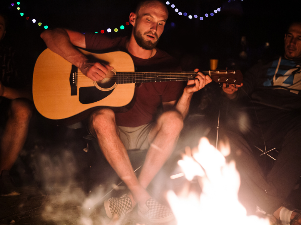 Young man playing acoustic guitar at a campfire
