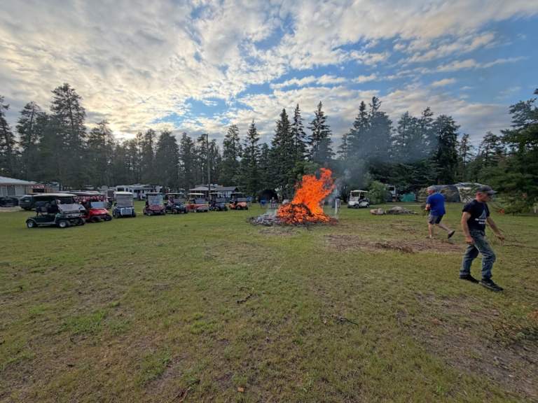Bonfire burning trimmed branches with the campers' golf carts lined up along the edge.